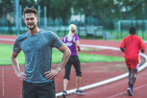 Young Caucasian man on athletic track, standing with hands on his hips, looking at camera © TheSupporter