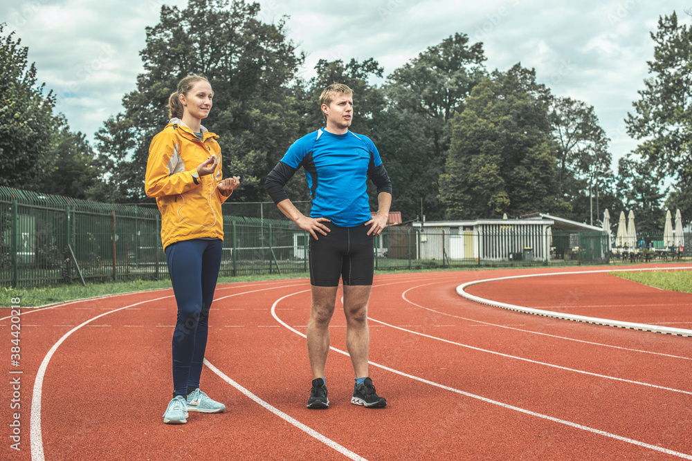 Fototapeta premium Young Caucasian woman and man observing athletic track while taking a training break
