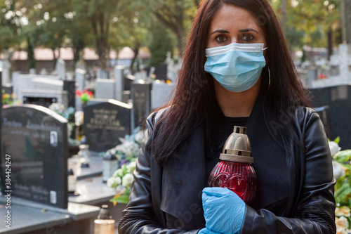 Konstfotografi A woman wearing a protective mask against the coronavirus COVID-19 SARS-CoV-2 holds a candle in her hand and visits her relatives at the cemetery