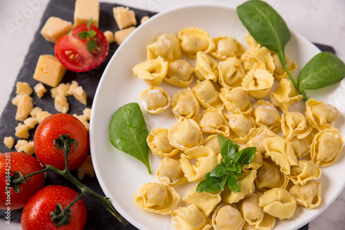 homemade raw tortellini on a white plate tomatoes, spinach and cheese. ingredients, italian cuisine