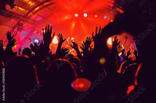 Abstract blur atmosphere: happy people enjoying outdoor music festival concert, raised up hands and clapping of pleasure, active night life concept, play of light and shadow on the stage