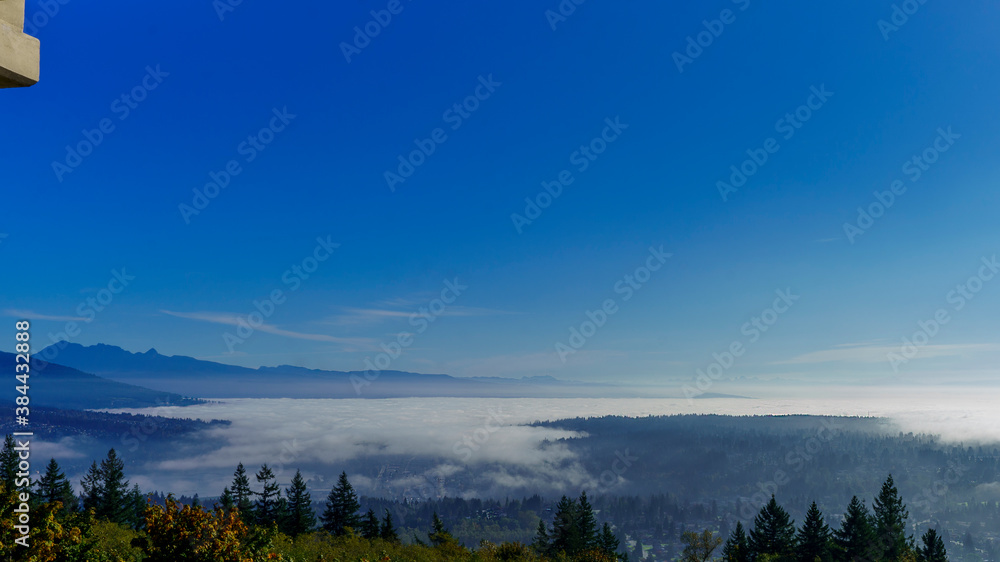 Clouds and mist overhanging valley floor in BC, with mountains in silhouette on horizon.