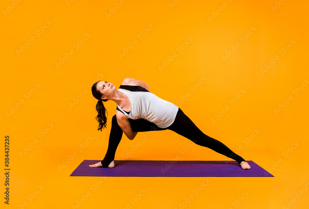 a woman performs yoga pose Utthita of Parsvakonasana on a purple Mat on orange background