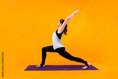 yoga woman performs a pose on a purple Mat on an orange background