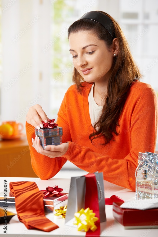 Young woman sitting at table wrapping gifts, looking down, smiling. Young woman sitting at table wrapping gifts, looking down, smiling.