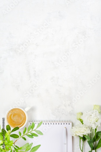 Cup of coffee, eustoma, pistachio greenery, notepad and pen on concrete background photo