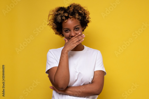 Young african woman giggles covering her mouth with hand, hiding her emotion photo