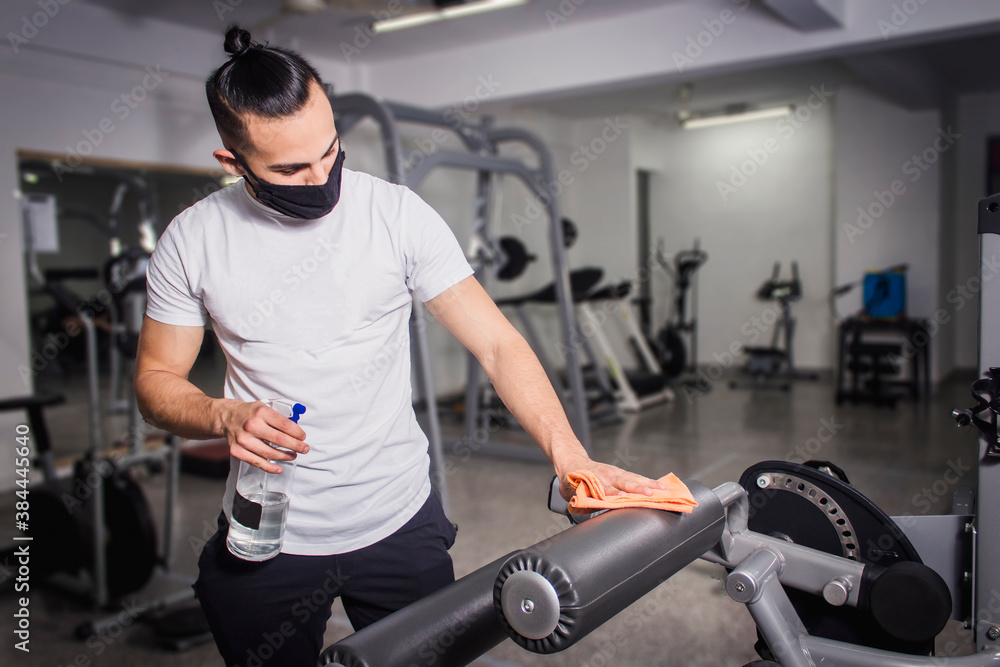 White man disinfecting the leg exercise machines. COVID-19 pandemic social distancing rules while working out White man disinfecting the leg exercise machines. COVID-19 pandemic social distancing rules while working out