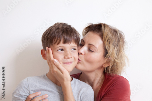 Portrait of happy smiling mom hugging her son sitting on a light background. Happy family concept. 