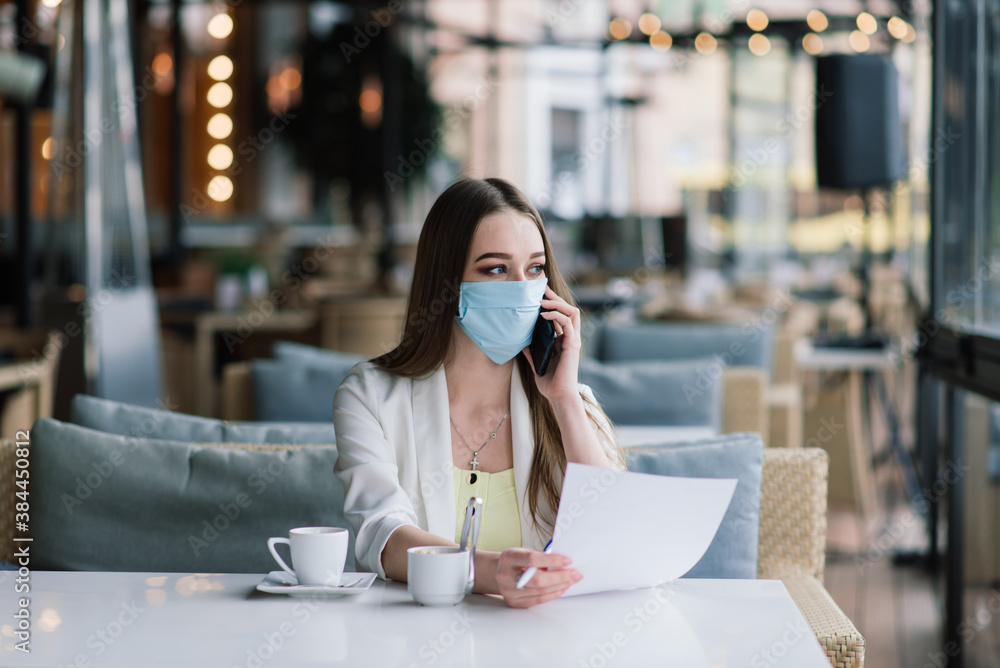 Serious woman with protective face mask looking at smart phone checking news on a cafe terrace Serious woman with protective face mask looking at smart phone checking news on a cafe terrace