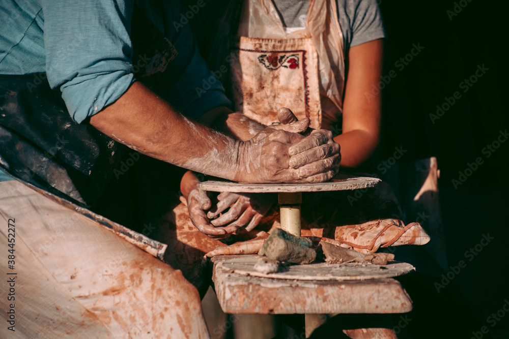 An experienced potter teaches an apprentice to work with clay and a potter's wheel