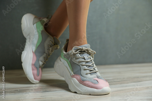 female legs in sports sneakers close-up on gray background