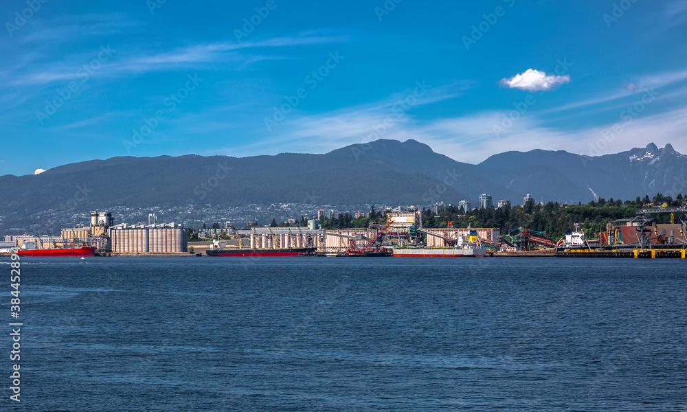 Ships under loading in the sea port of North Vancouver on the background of mountain range and blue sky