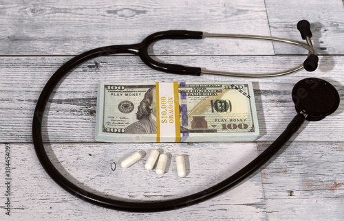 Stack of play money $100 bills , some pills surrounded by a stethoscope. .High medical cost concept.