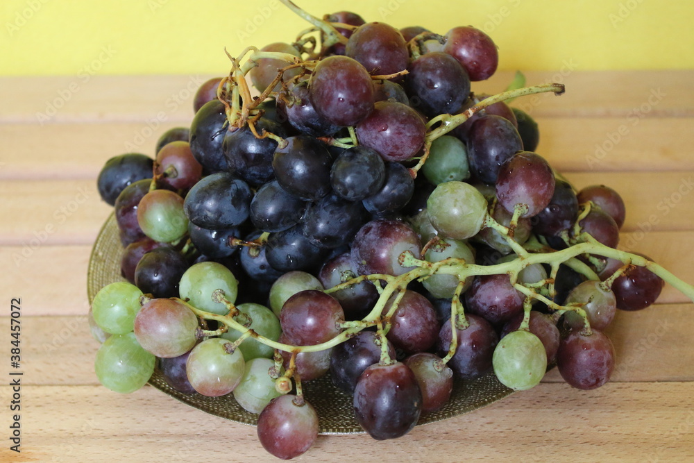 Grapes on a plate on a wooden base and a yellow background Grapes on a plate on a wooden base and a yellow background
