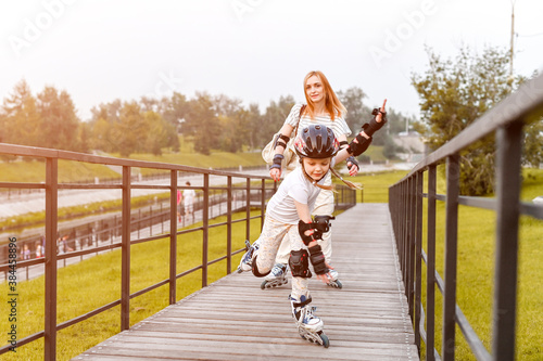 Young mother and her daughter rollerskating in summer day