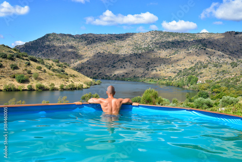 Man relaxing in a swimming pool looking and the Douro Valley landscape