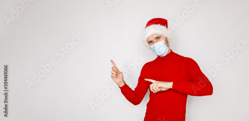 Christmas during pandemic of COVID-19 Coronavirus. Man wearing surgical face mask and Santa hat. Male model wearing red sweater on white isolated background. Place for copy banner text seasonal Sales
