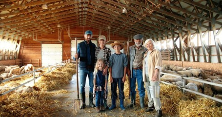 Portrait of happy Caucasian family of three generations standing in shed with livestock and smiling. Old parents with children and grandchildren in stable. Farmers with kids at farm. Zooming out.