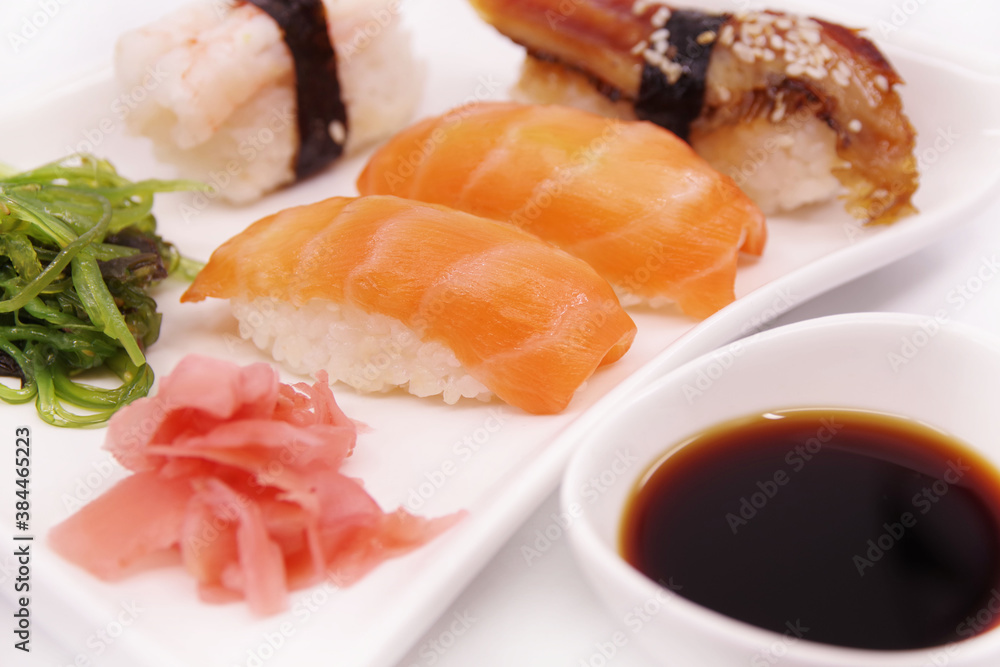 Japanese sushi food on a white plate, served with ginger and seaweed salad. Salmon nigiri, shrimp nigiri, unagi nigiri Japanese sushi food on a white plate, served with ginger and seaweed salad. Salmon nigiri, shrimp nigiri, unagi nigiri