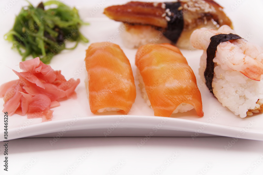 Japanese sushi food on a white plate, served with ginger and seaweed salad. Salmon nigiri, shrimp nigiri, unagi nigiri Japanese sushi food on a white plate, served with ginger and seaweed salad. Salmon nigiri, shrimp nigiri, unagi nigiri