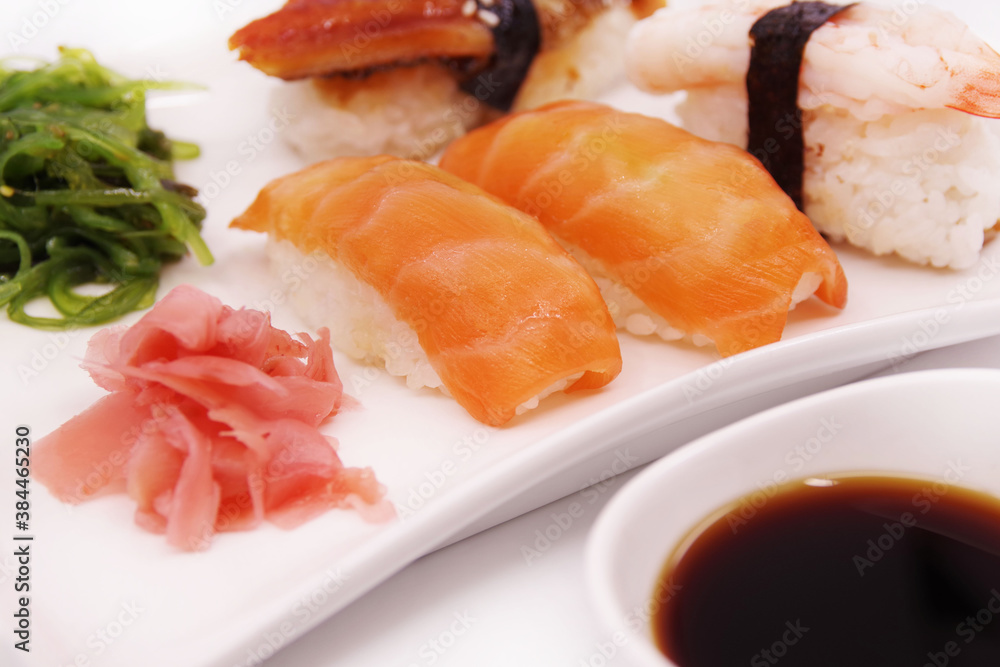 Japanese sushi food on a white plate, served with ginger and seaweed salad. Salmon nigiri, shrimp nigiri, unagi nigiri