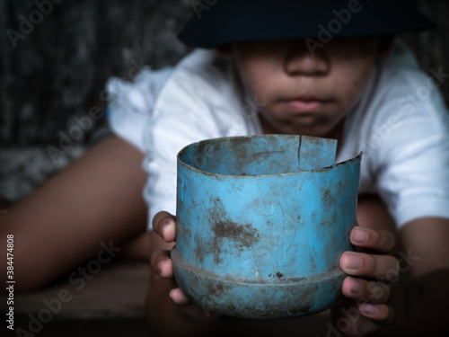Child or poor homeless holding plastic bowl with hungry and asking help food donation from traveler on street at the city. Unidentified homeless child begging on street. Shelter concept.