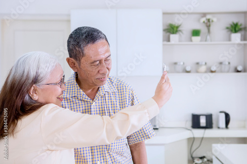 Happy old couple taking selfie together in kitchen