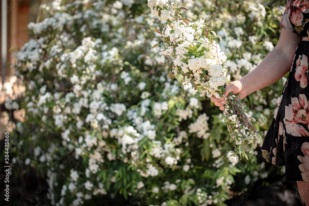 Woman wearing floral dress holding bunch of white flowers in beautiful cottage garden