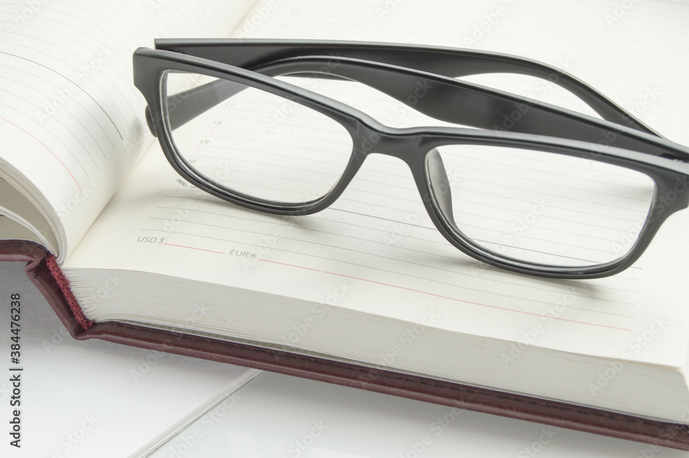 Stylish black reading glasses on an open diary, close-up banner