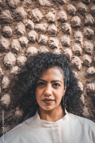 Beautiful smiling young latin natural woman, texture wall, afro curly hair, seriedad photo