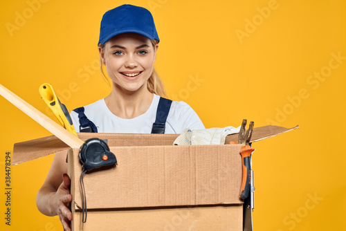 Woman with a box of construction tools and in a cap on a yellow background repair construction industry