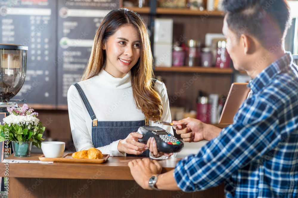 Asian customer man paying with credit card via contactless nfs technology to Asian Barista of Small business owner at the table in coffee shop, Small business owner and startup in coffee shop concept Asian customer man paying with credit card via contactless nfs technology to Asian Barista of Small business owner at the table in coffee shop, Small business owner and startup in coffee shop concept