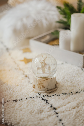 Magic glass snow globe with deer and a garland on a fluffy carpet in a bright interior.