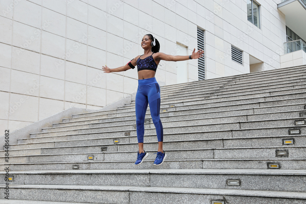 Positive pretty young Black sportswoman spreading arms and jumping on stairs