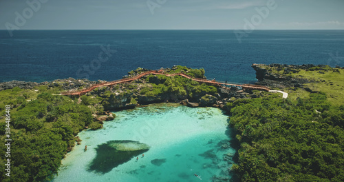 Tropical resort at turquoise Weekuri lake landscape with green jungle forest and grass. People relax and swim in salt water lagoon at neighboring sea bay cliff coast of Indonesia, Asia