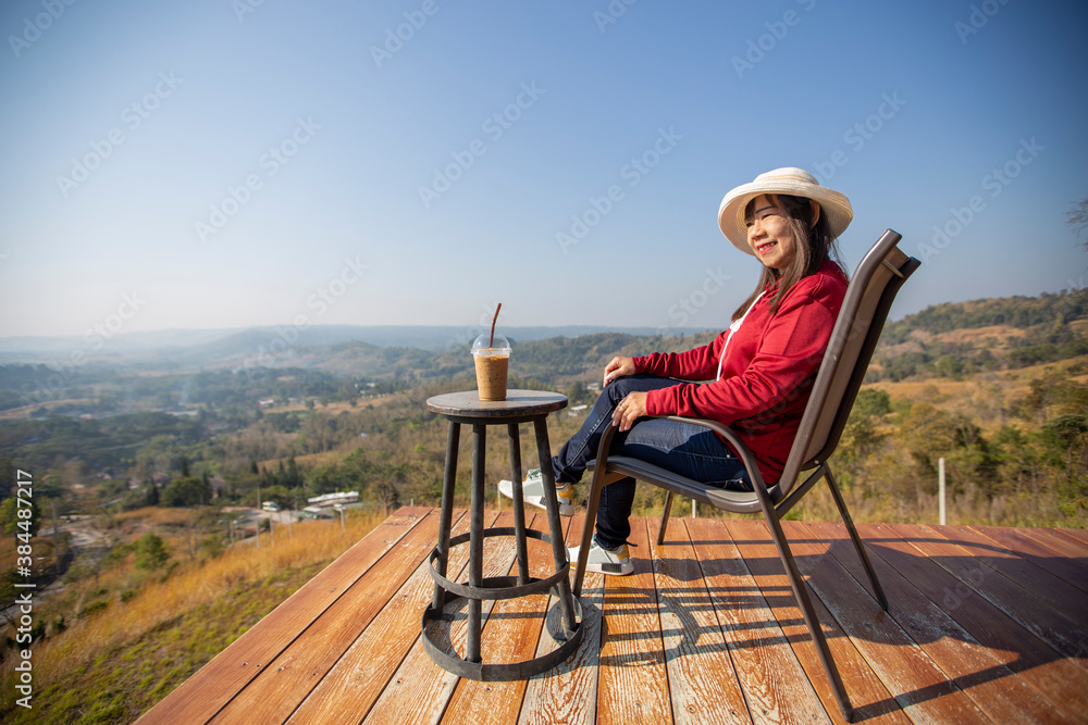 The elderly Asian woman is sitting on a wooden chair waiting to watch the sunrise over mountain in the morning at petchaboon province , Thailand.