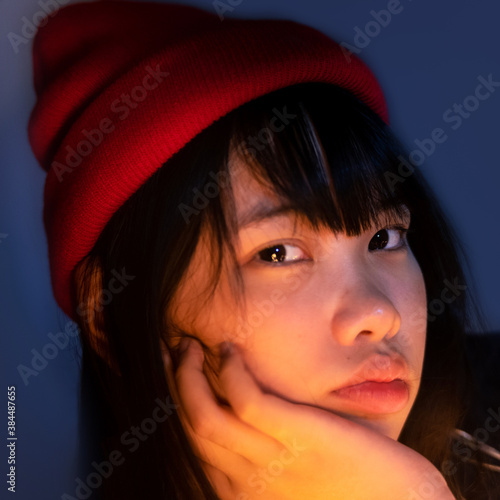 Canvas Print A closeup of an attractive Asian girl wears a red beanie in isolated blue backgr