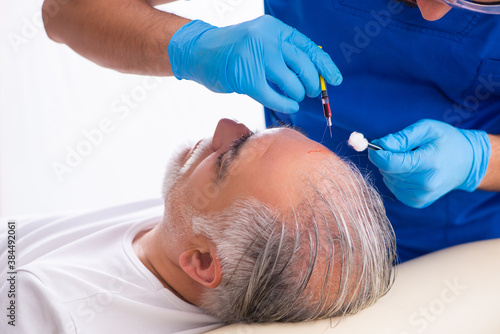 Old man visiting young male doctor in hair transplantation conce