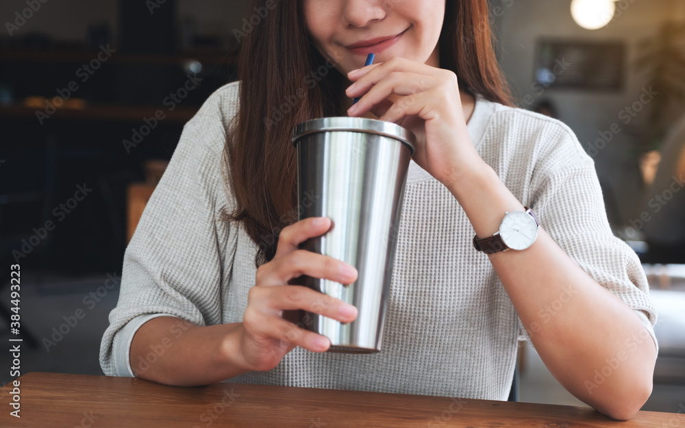Closeup image of a beautiful asian woman drinking coffee in stainless steel cup - obrazy, fototapety, plakaty 