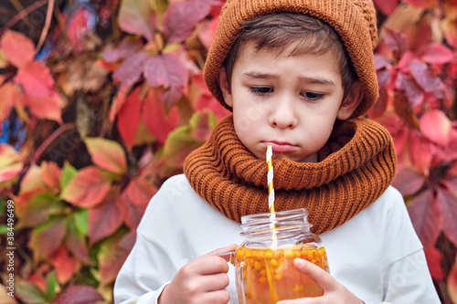 cute fashionable boy holding a sea buckthorn drink on a background of wild grapes. portrait of sad boy, autumn blues concept