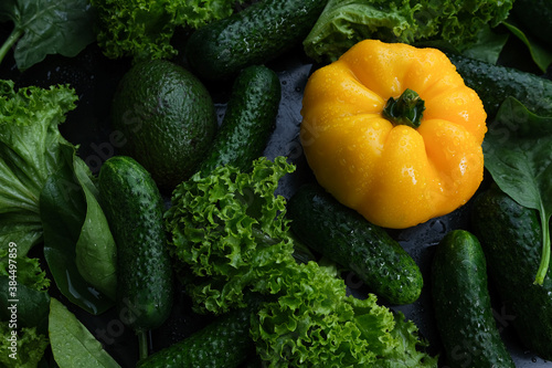 Fresh vegetables, yellow bell peppers, cucumber and salad on a black background.