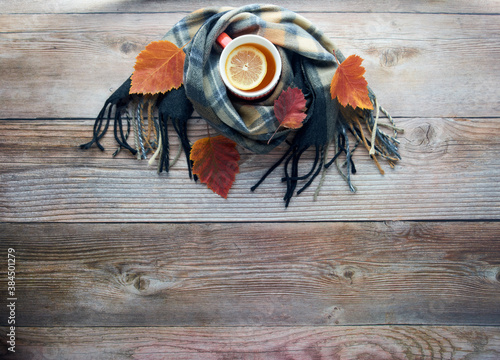 Autumn leaves, cup of black tea with lemon slice and warm scarf on wooden table. Fall season, leisure time, Sunday relaxing, teatime and still life concept. Selective focus. Top view, copy space..