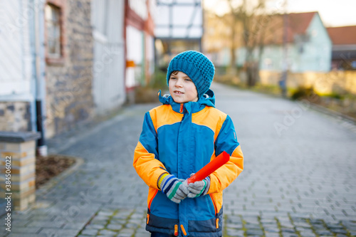 Little school kid boy of elementary class walking to school on cold winter day. Happy child having fun on a city street. Student with backpack in colorful winter clothes holding things for project