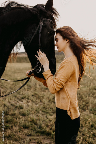 Young woman hugging a black friesian horse, outdoors.