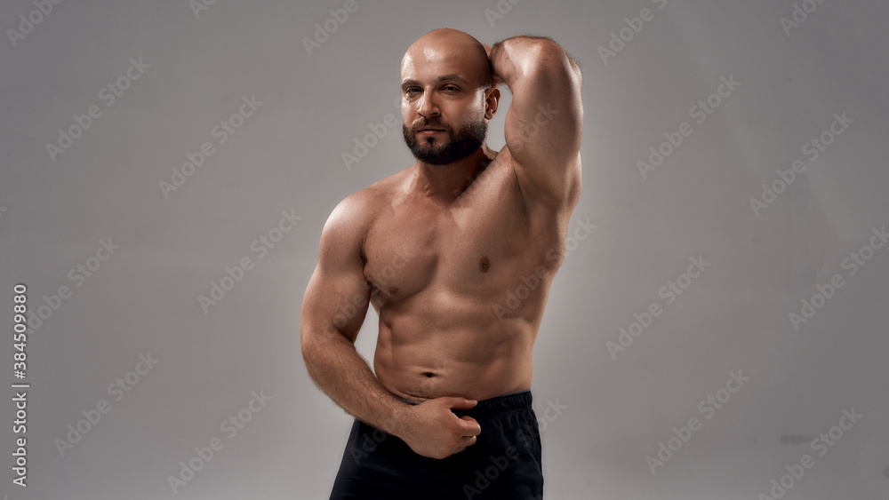 Pumping up muscles. Strong athletic caucasian man bodybuilder showing his perfect body and looking at camera while posing shirtless isolated over grey background