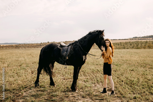 Young woman hugging a black friesian horse, outdoors, in a field.