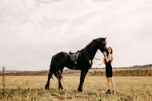 Young woman hugging a black horse, outdoors, in a field.