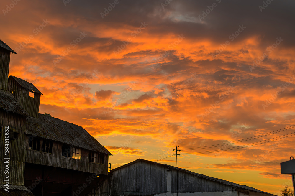 Landscape photo in the orange setting sun of abandoned old buildings in autumn against the backdrop of a dramatic sky
