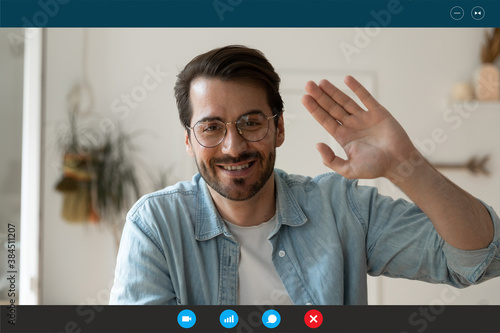 Close up headshot screen view portrait of smiling young Caucasian man in glasses wave greet talk speak on video call. Happy male enjoy online communication, have webcam virtual digital conference.